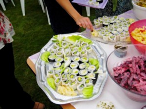 A potluck table at a wedding with rolled sushi and other foods.