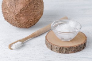 Coconut oil in a small bowl next to a coconut and a toothbrush.