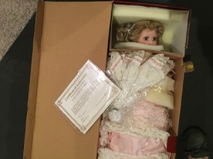 Determining the Value of a Porcelain Doll Collection - doll wearing a pink dress wrapped in plastic in a cardboard box