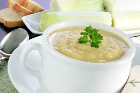 A cup of soup next to a platter of leeks and some bread.