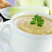 A cup of soup next to a platter of leeks and some bread.