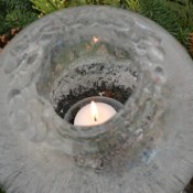 Round ice candle surrounded by greenery.