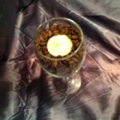 A wine glass filled with coffee beans with a tealight candle.