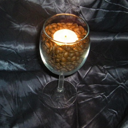 A wine glass filled with coffee beans with a tealight candle.