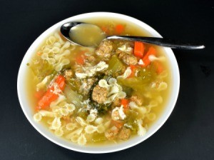 A bowl of Italian Wedding soup with meatballs, pasta, escarole and other veggies.