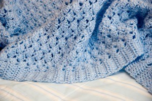 A blue blanket crocheted with a shell pattern.