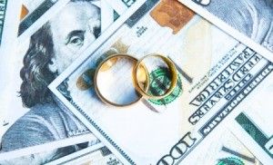 A pair of golden wedding bands on top of a spread out hundred dollar bills.
