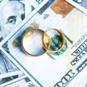 A pair of golden wedding bands on top of a spread out hundred dollar bills.