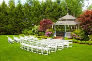 Outdoor wedding with white folding chairs outside near a gazebo.