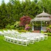 Outdoor wedding with white folding chairs outside near a gazebo.