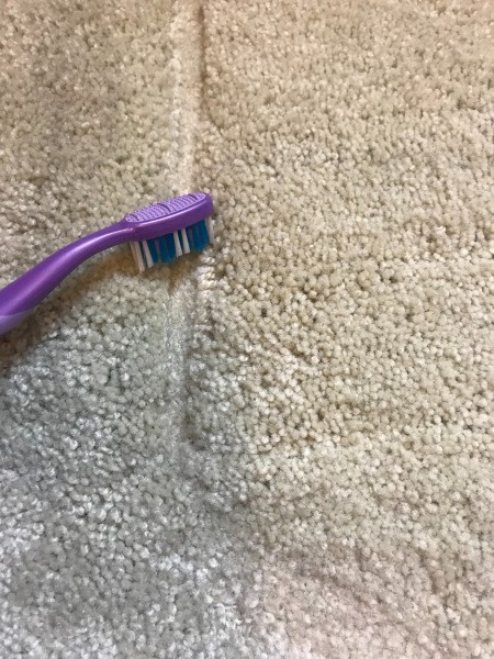 Using a toothbrush to fluff a dent in a carpet.