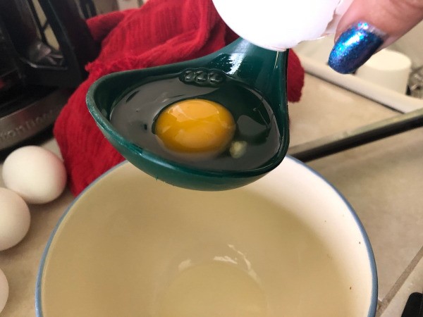 A cracked egg in a spoon, to be place in the poaching water.