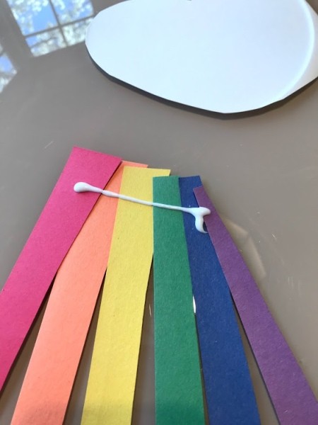 Making a Paper Plate Rainbow  - add glue to the paper strips