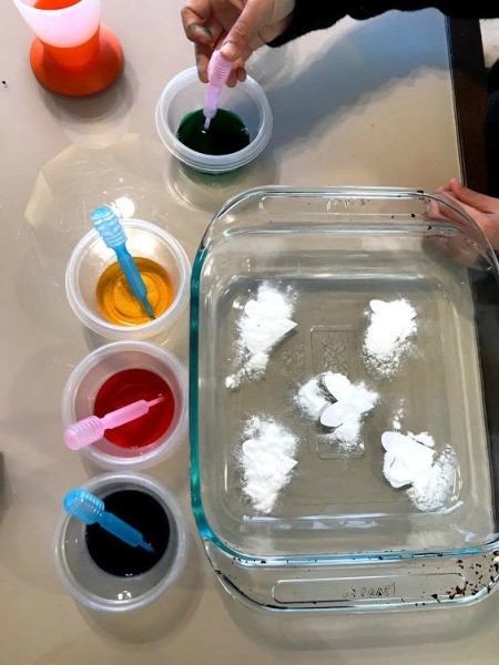 Crafting Supplies from Baking Soda and Vinegar Experiment - glass dish, cups of vinegar and food coloring, with child's hand using pipette to suck up some dye