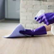 A pair of gloved hands cleaning a table with a spray bottle and a rag.