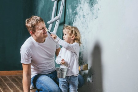 A little girl helping her father primer a wall.