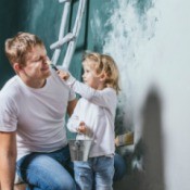 A little girl helping her father primer a wall.