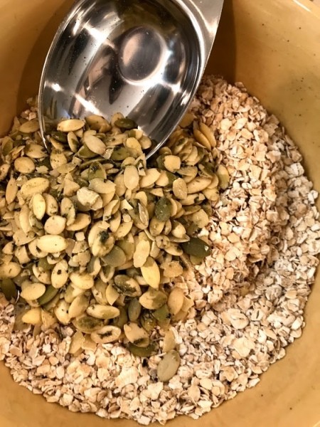 adding pumpkin seeds to oats in bowl