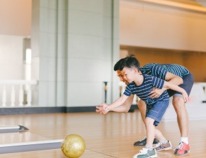 Dad helping son bowl.