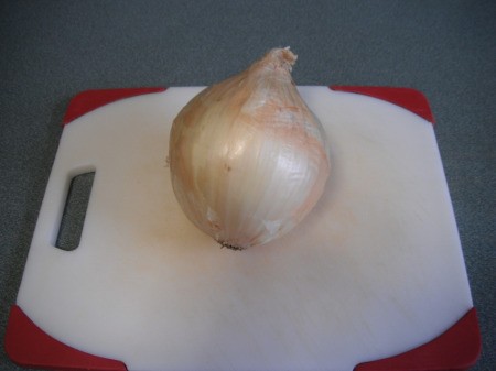 A whole onion with peel on a cutting board.