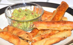 A plate of fried beef taquitos served with guacamole.