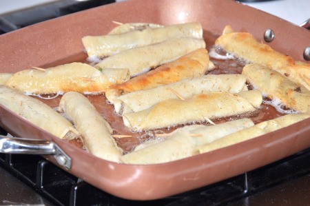 Cooking taquitos in a frying pan.