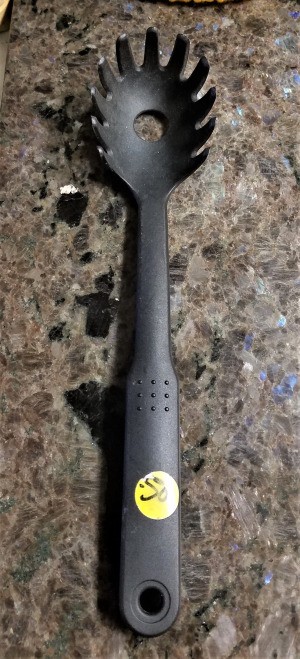 A black spaghetti spoon with tines and a hole in the middle.