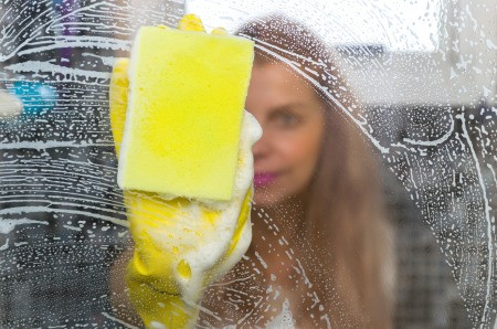 A woman washing a window with lots of soapy streaks.