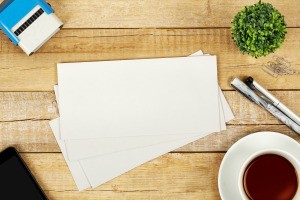 Several envelopes on a desk with other supplies around.