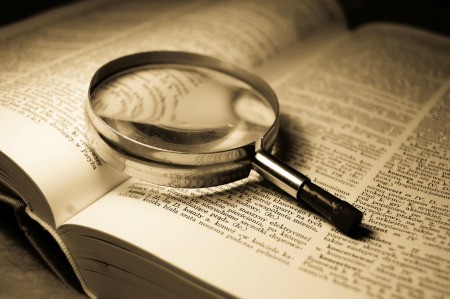 An open dictionary with a magnifying glass.