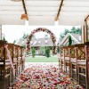 Wedding venue with wooden chairs, flower petal path leading to a flower arch.