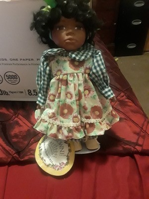 Value of a Crowne Porcelain Doll - African American doll wearing a floral pinafore dress with a checkered blouse