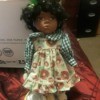 Value of a Crowne Porcelain Doll - African American doll wearing a floral pinafore dress with a checkered blouse