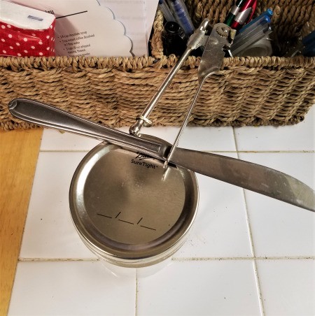 How to Reuse Your Canning Jar Lids for Crafts - butter knife on edge of canning jar lid and lid opener end of can opener in place