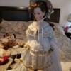 Identifying a Porcelain Doll - doll wearing a hat and gold trimmed fancy long white dress with lace around the hem