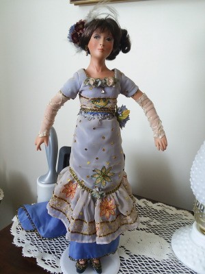 Value of a Kathleen Hill Porcelain Doll - doll wearing a long blue dress with ruffled bottom over a dark blue underskirt