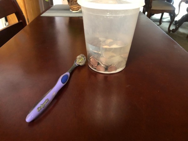 Coins soaking in a cleaning bath, next to a toothbrush.