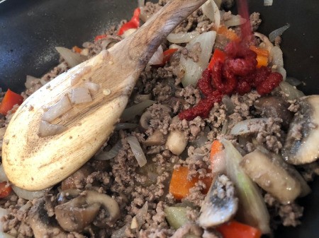 mixing tomato paste to ground beef with veggies