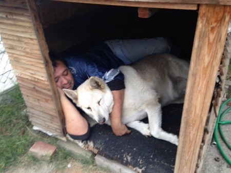 A man and his dog sleeping together in a large dog house.