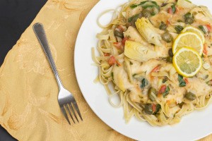 A plate of chicken piccata served over noodles.