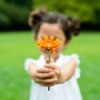 A child holding a flower out to the viewer.