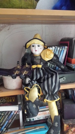 Identifying a Porcelain Doll - doll sitting on a shelf, wearing a black and gray sort of clown outfit with pointed hat