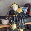Identifying a Porcelain Doll - doll sitting on a shelf, wearing a black and gray sort of clown outfit with pointed hat