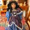 Identifying a Porcelain Doll - dark haired doll wearing a blue dress with a floral over bodice and skirt