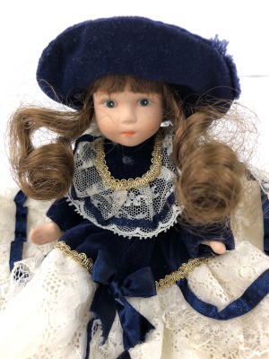 Identifying a Porcelain Doll - doll wearing a white lace dress with a dark blue jacket and matching hat