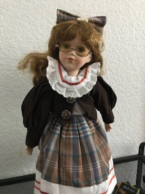 Identifying a Porcelain Doll - doll wearing a plaid dress with a dark jacket and matching hair bow, plus eyeglasses