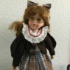 Identifying a Porcelain Doll - doll wearing a plaid dress with a dark jacket and matching hair bow, plus eyeglasses