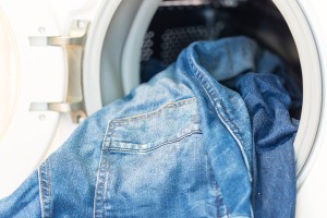 Dirty jeans hanging out of a washing machine.