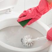 Person wearing pink rubber gloves cleaning a toilet with a sponge and a brush.