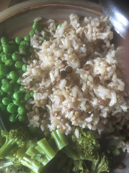 A plate of cooked lentils and brown rice with veggies.